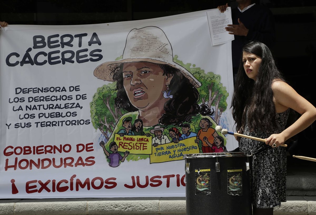 Una activista en Ecuadro ejecuta un instrumento musical frente a una pancarta con la imagen de la hondureña Berta Cáceres. (Foto Prensa Libre: AP).