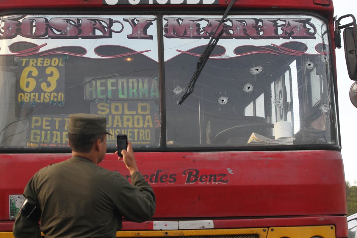 Un soldado documenta los daños al vidrio frontal del autobús, atacado a balazos en la zona 13. (Foto Prensa Libre: Érick Ávila)