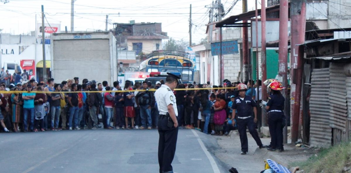 Un oficial de PNC observa el cadáver del ayudante de bus que fue ultimado en Chimaltenango. Al fondo, decenas de curiosos en la escena. (Foto Prensa Libre: Víctor Chamalé)