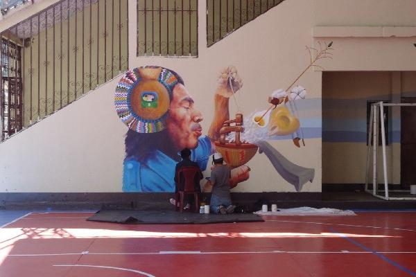 Dos artistas trabajan en la obra Naooj Tinamit, en la pared del salón municipal.