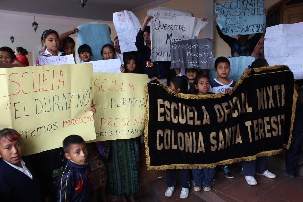 Niños portan carteles con leyendas de solicitud de maestros.