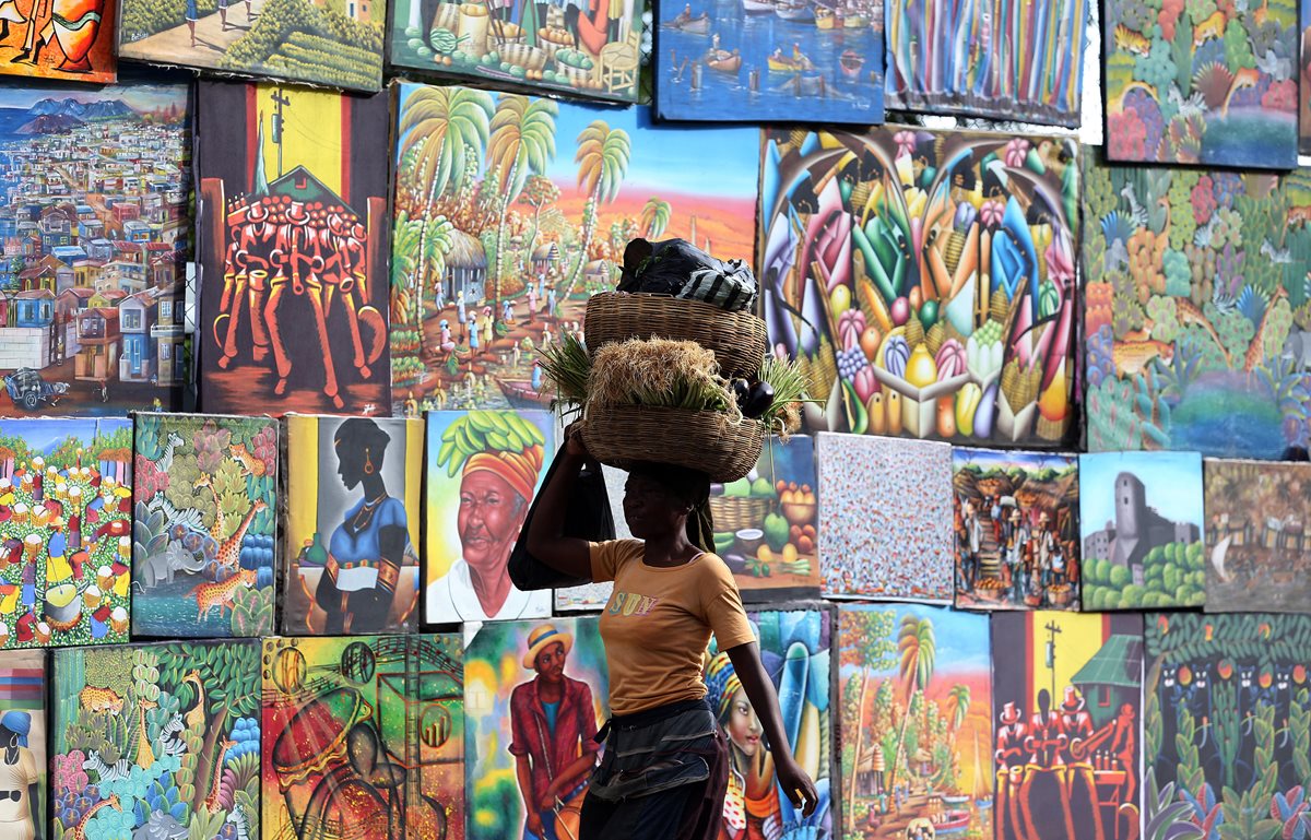Una mujer camina cargando una cesta junto a un puesto de callejero de venta de pinturas en Puerto Príncipe, Haití. (Foto Prensa Libre: EFE).