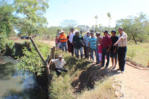 Vecinos muestran el tramo donde un río socava el camino, por lo que es necesario construir un muro para evitar que lo siga destruyendo.