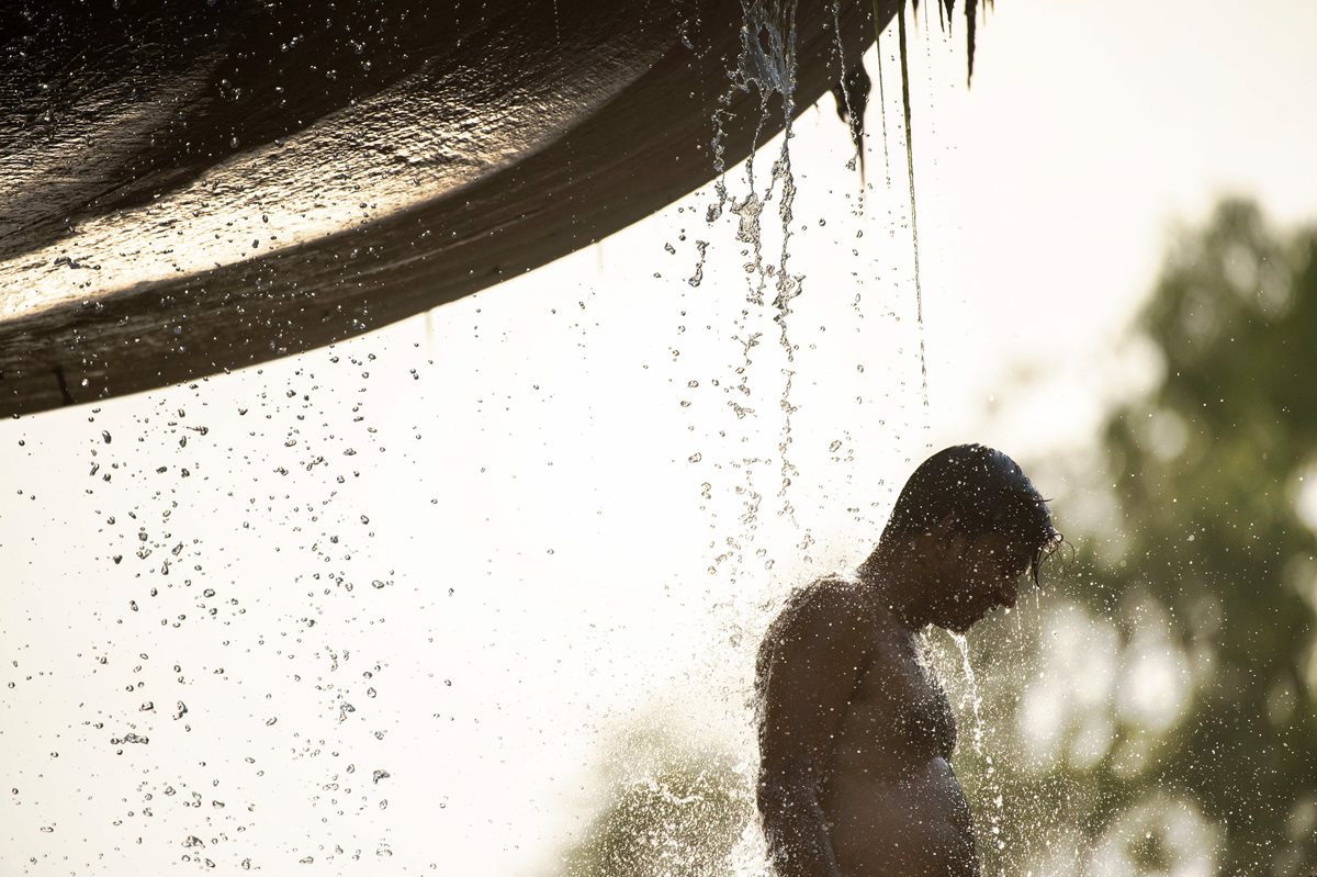 Un joven se refresca por el intenso calor en una fuente pública en Nueva Delhi, India. (Foto Prensa Libre: AFP).