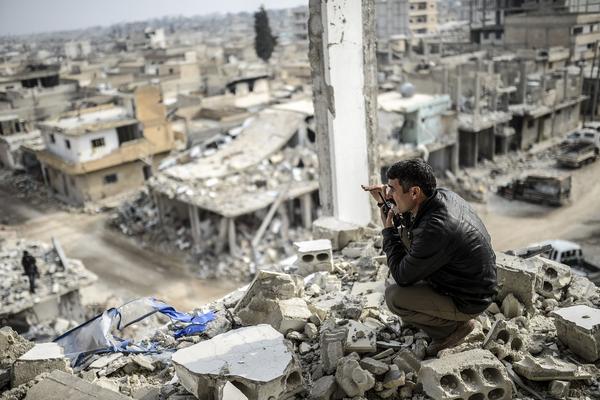 Un curdo habla por radio, al fondo la ciudad de Kobane en ruinas. (Foto Prensa Libre: AFP).