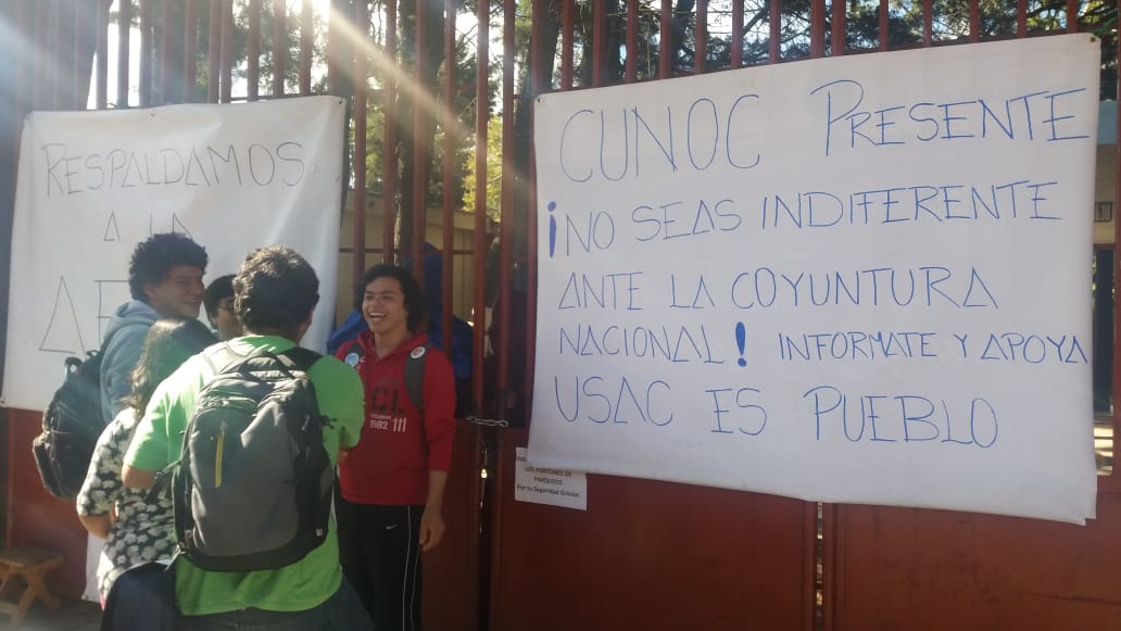 Un grupo de estudiantes lee los carteles que los encapuchados colocaron en una de las puertas de ingreso. (Foto Prensa Libre: Fred Rivera)