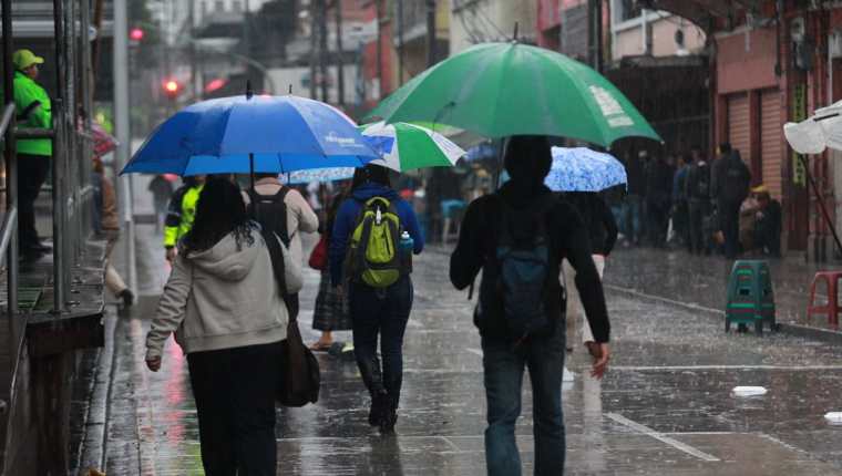Guatemaltecos se cubren de la lluvia mientras caminan por la zona 1 capitalina. (Foto Prensa Libre: Hemeroteca PL)