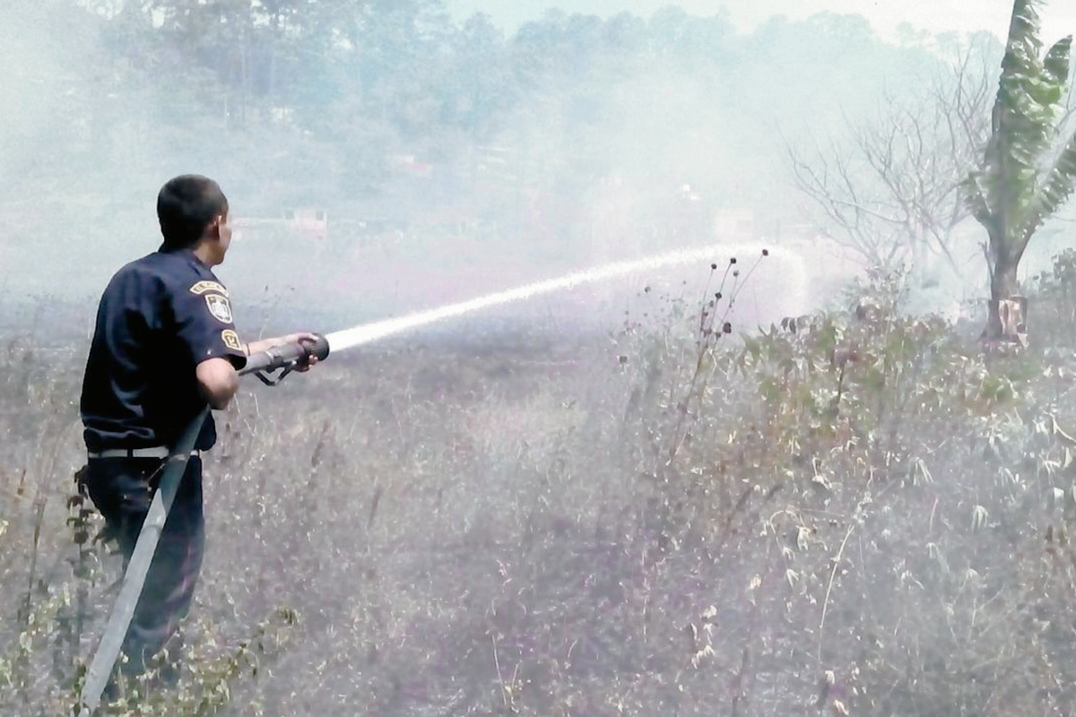 El bombero  Erick Morales lanza agua sobre los pastizales para que el fuego no avance. (Foto Prensa Libre: Víctor Chamalé)