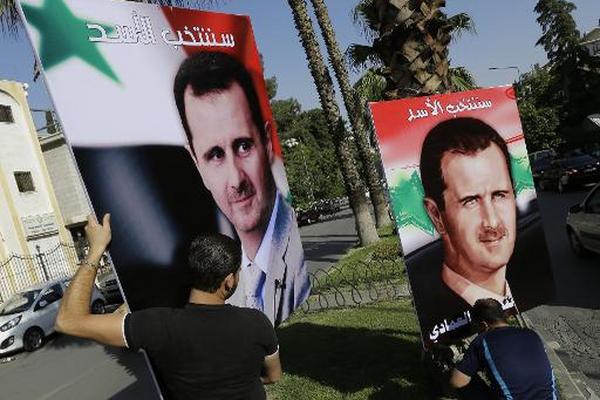 Dos hombres cuelgan carteles del presidente sirio, Bachar Al Asad. (Foto Prensa Libre: AFP).