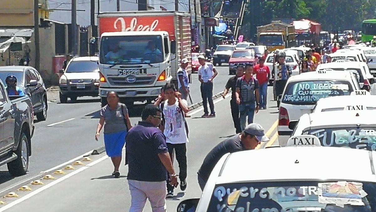 Las personas caminan sobre la vía del Transmetro para llegar a sus labores.