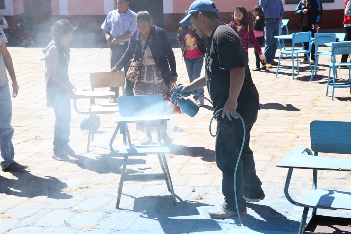 Padres de familia y estudiantes pintan escritorios de un aula de Escuela Soledad España, en Xelajú. (Foto Prensa Libre: María José Longo)