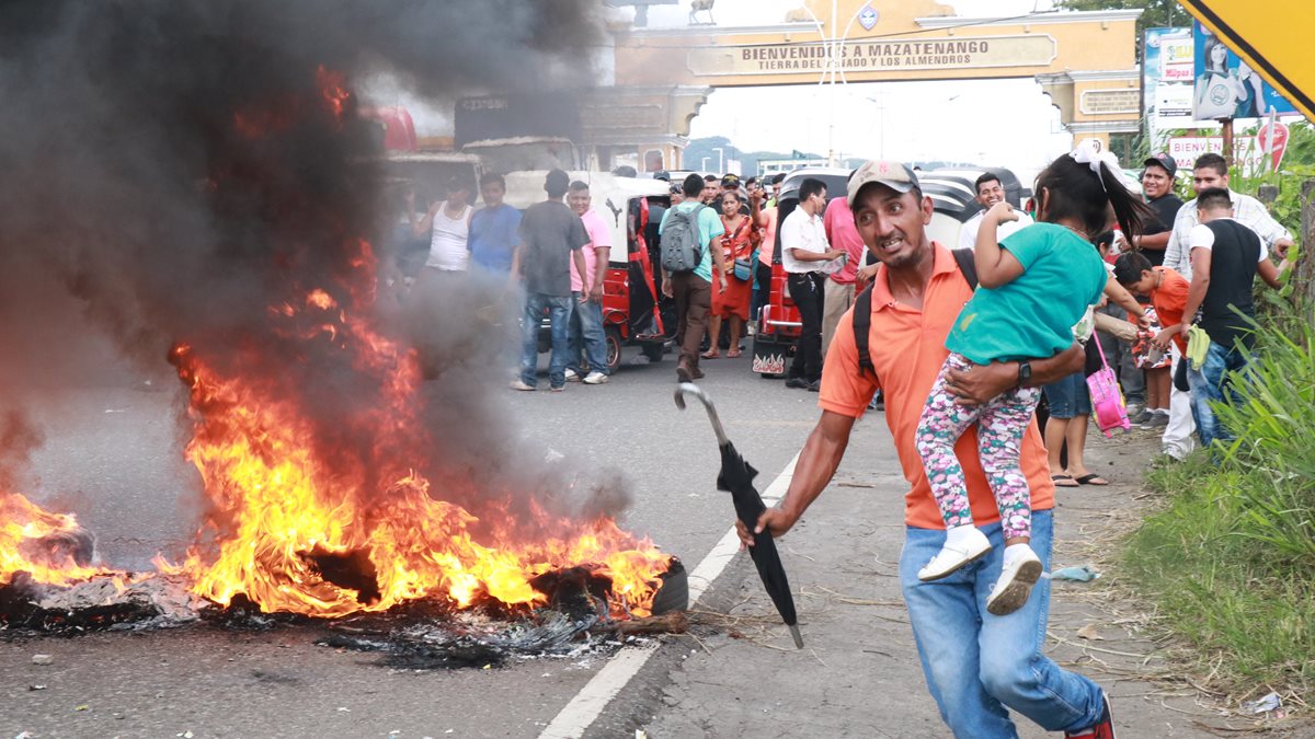 Un hombre carga a su hija y huye de la protesta de mototaxistas que quemaron llantas en la ruta al Pacífico. (Foto Prensa Libre: Cristian Icó)