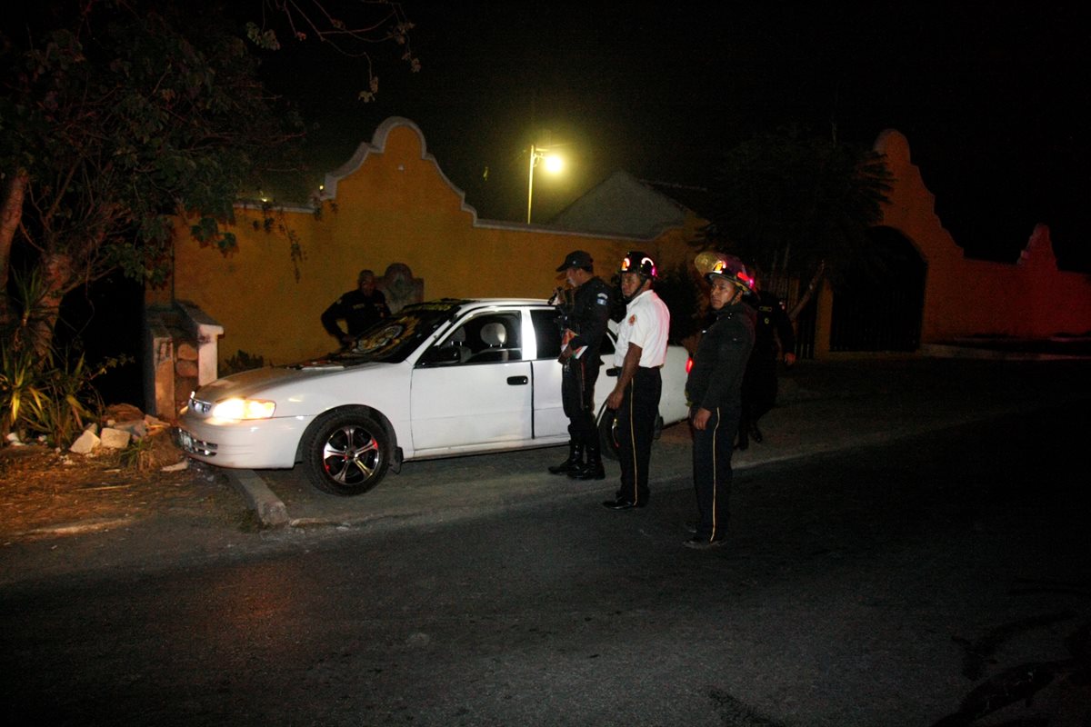 Agentes de la PNC y Bomberos Voluntarios observan el vehículo en el que quedaron los cadáveres de las víctimas. (Foto Prensa Libre: Renato Melgar)