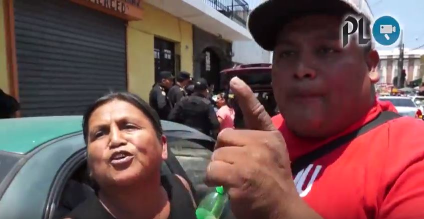 El sujeto de camisa roja golpea dos veces la cámara de la reportera, la intimida junto a la mujer de traje negro. (Foto Prensa Libre)