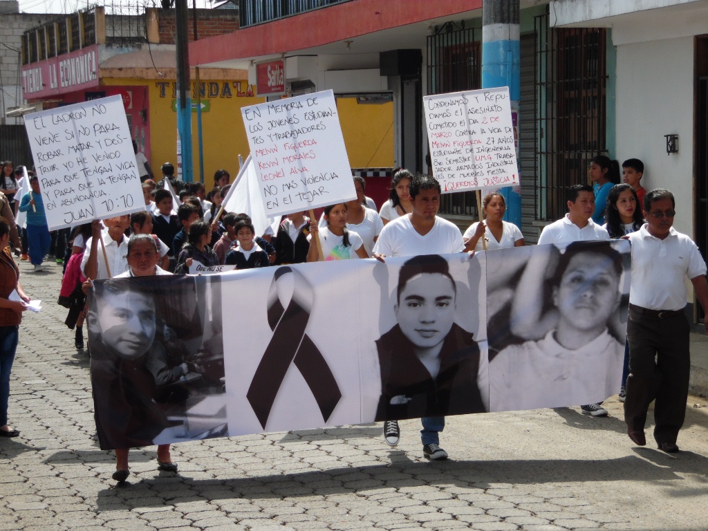 Pobladores portan manta con el rostro de los tres jóvenes ultimados recientemente en El Tejar. (Foto Prensa Libre: José Rosales).