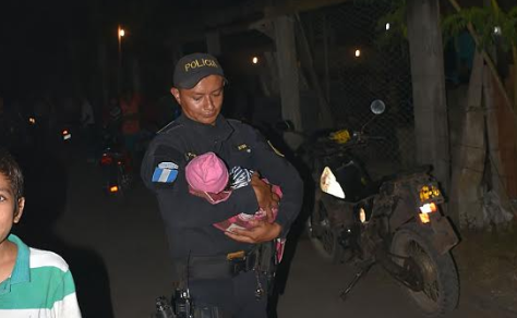 Agente de la PNC carga a la menor luego de fuera localizada en Puerto San José. (Foto Prensa Libre: Enrique Paredes).