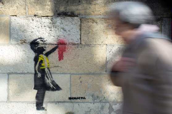 Una mujer camina  junto a una obra parecida al trabajo de Banksy titulado "Niña con Globo" en la fachada de un edificio en Burdeos, Francia. EFE