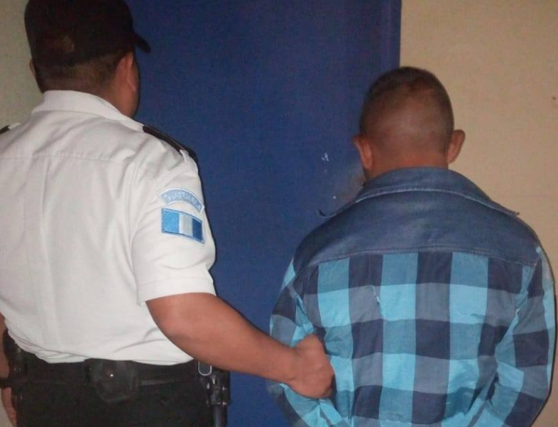 Juan Tista Pérez, quien pretendía agredir a su hijo, es custodiado por una agente de la PNC. (Foto Prensa Libre: PNC). 

