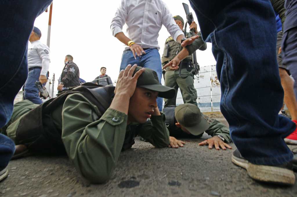 Dos soldados venezolanos yacen en el suelo mientras son detenidos por la policía colombiana después de conducir a Colombia en un vehículo blindado desde el lado venezolano