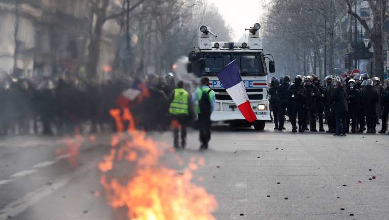 Los manifestantes del movimiento Chalecos Amarillos que sostienen una bandera francesa se enfrentan a los policías antidisturbios franceses durante los enfrentamientos como parte de la manifestación. (Foto Prensa Libre: EFE).