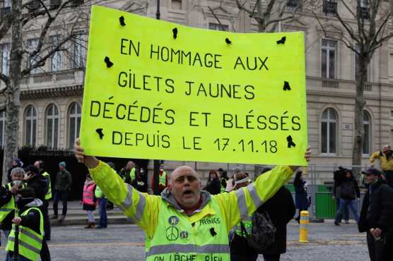 Un manifestante de sostiene un cartel que dice "En homenaje a los manifestantes de Yellow Vests que murieron y resultaron heridos desde el 17.11.18" en los Campos Elíseos de París el 16 de marzo de 2019. Foto Prensa Libre: AFP 