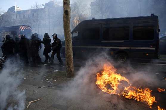 La policía antidisturbios corre en los Campos Elíseos cerca de un incendio durante la manifestación en Francia. Foto Prensa Libre: EFE