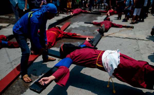 Devotos cristianos cubren sus rostros mientras esperan en sus cruces durante un acto de crucifixión en Filipinas. Foto Prensa Libre: AFP
