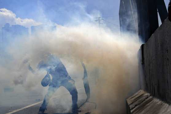 Una persona trata de salir de las nubes de humo que lanzaron las tropas fieles a Nicolás Maduro. Foto Prensa Libre: AFP 
