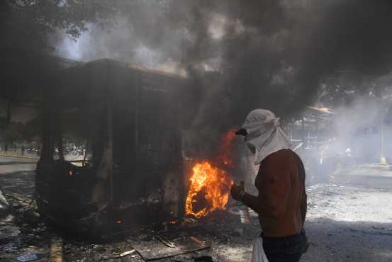 Un manifestante de la oposición es visto junto a un autobús del gobierno incendiado durante los enfrentamientos con soldados leales al presidente venezolano Nicolás Maduro. Foto Prensa Libre: AFP 