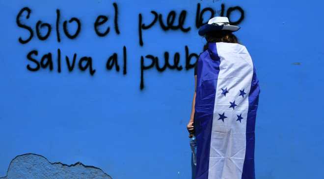 Un manifestante permanece al lado de un graffiti durante una manifestación en Tegucigalpa. Foto Prensa Libre: AFP 