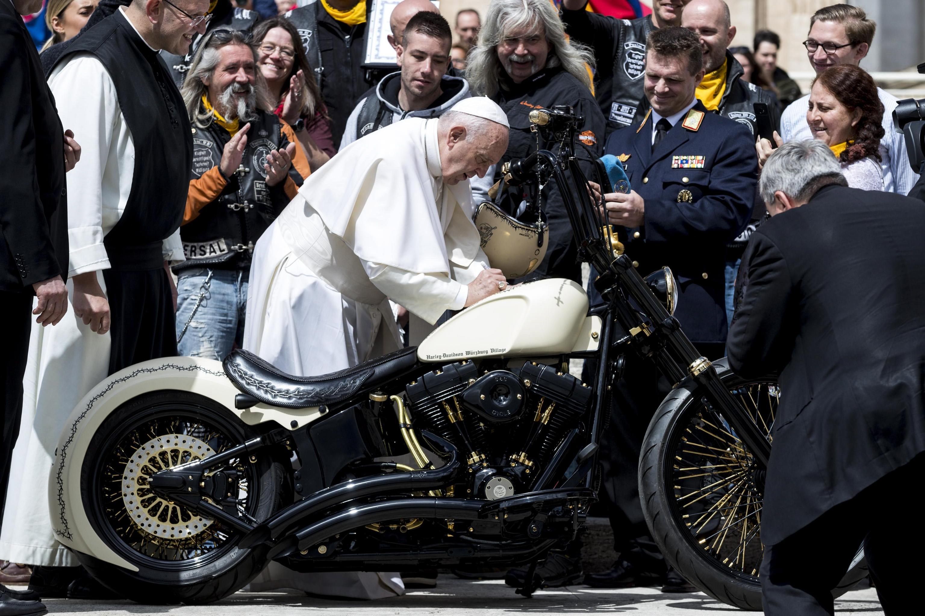 El papa Francisco firma en el depósito de una Harley Davidson mientras saluda a miembros de la asociación de motociclistas. (Foto Prensa Libre: EFE)