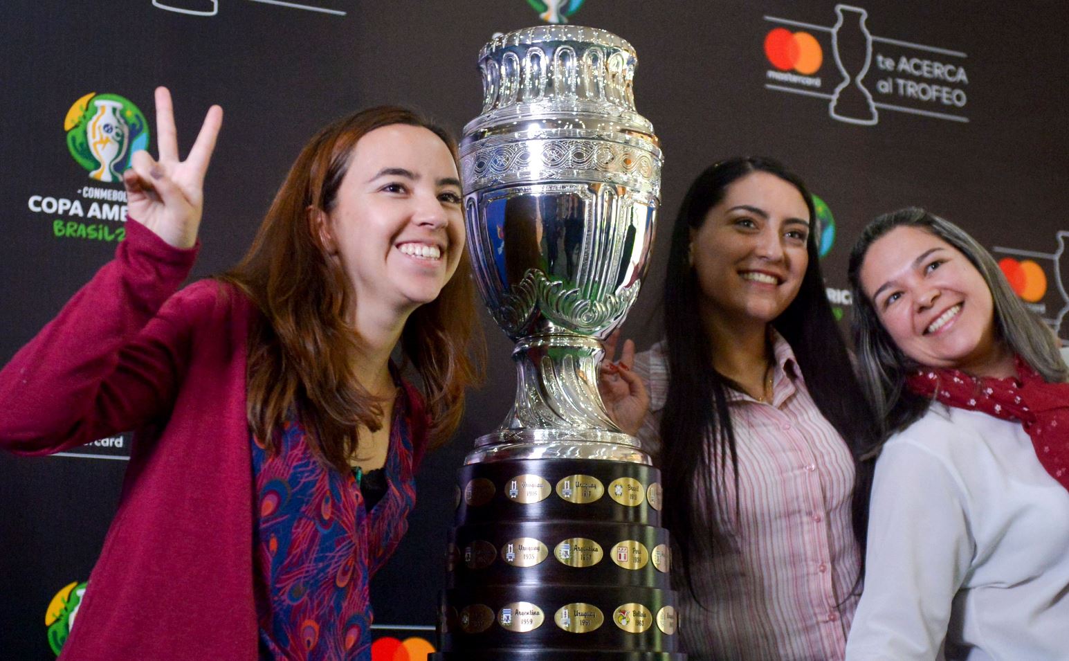 Varias aficionadas posan junto al trofeo de la  Copa América en Bogotá. (Foto Prensa Libre: AFP).