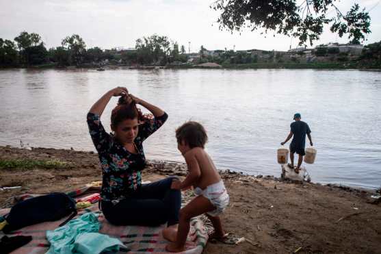 Una mujer hondureña y su hija esperan en la orilla del río para continuar su viaje. Foto Prensa Libre: AFP 