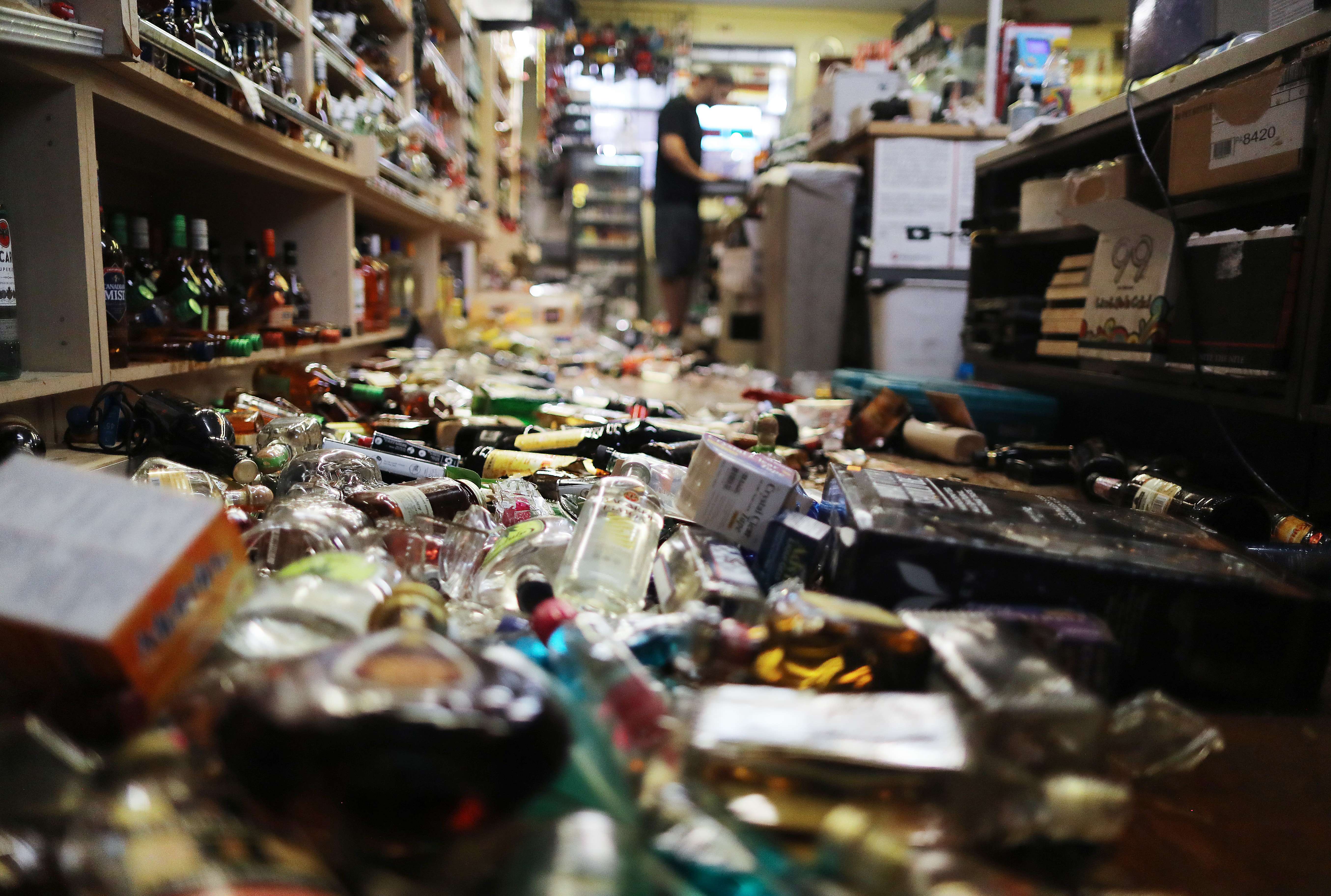 Un empleado trabaja en la caja registradora cerca de botellas rotas esparcidas en el piso, luego del sismo de magnitud 7.1 que afectó California. (Foto Prensa Libre AFP).