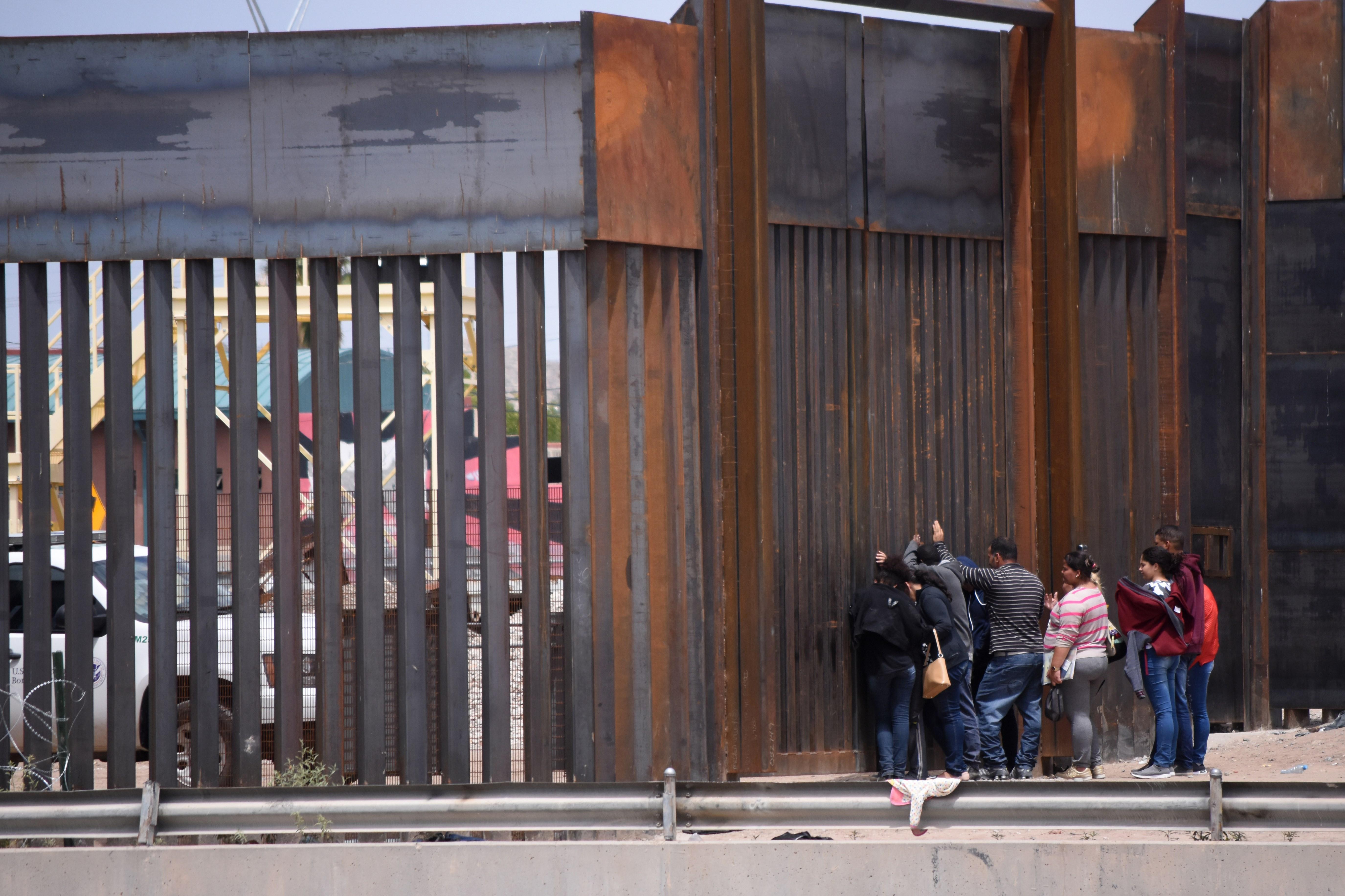 Migrantes centroamericanos se asoman por el muro fronterizo para entregarse a las autoridades estadounidenses. (Foto Prensa Libre EFE)