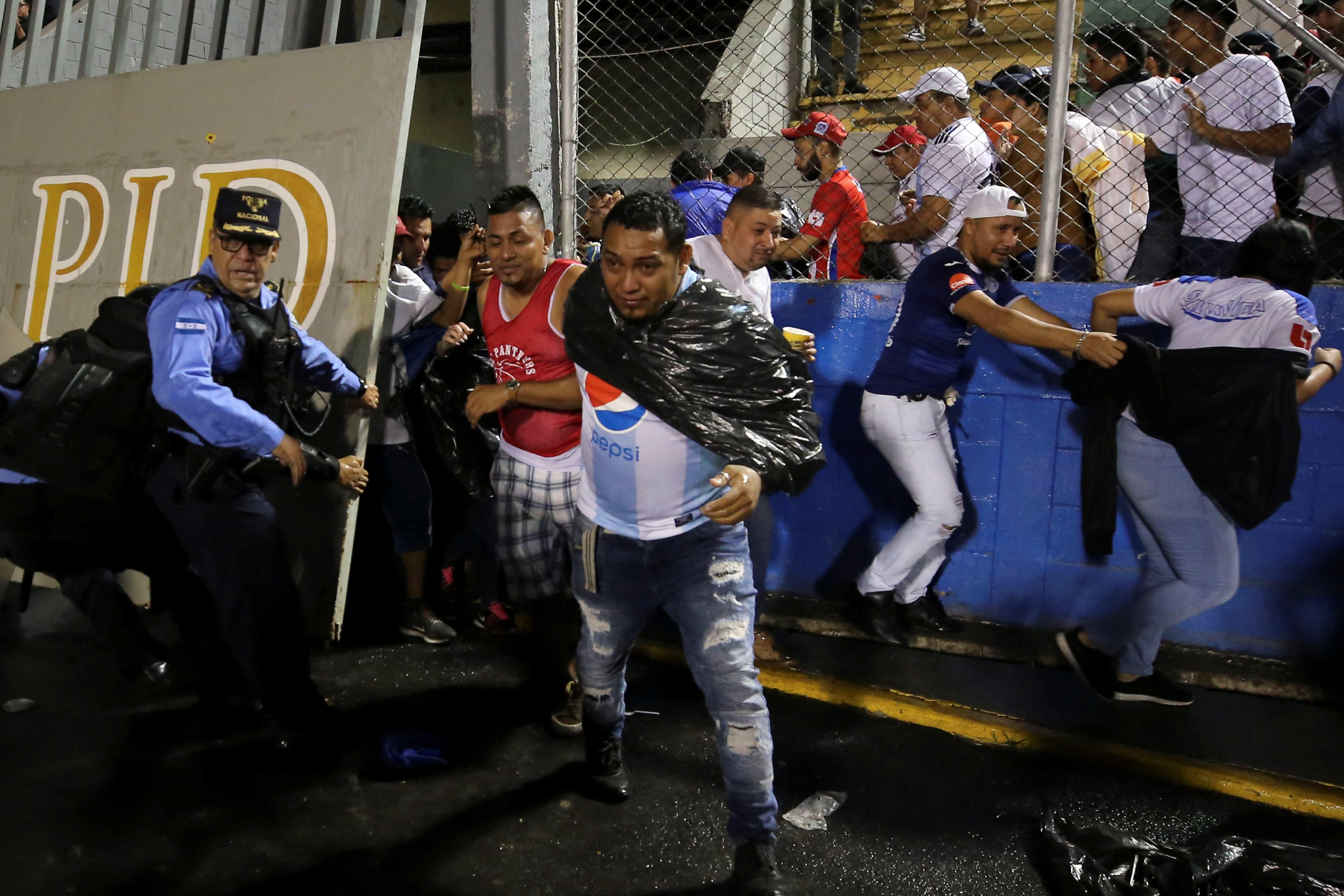 Aficionados ingresan al campo y se protegen de los gases lacrimógenos lanzados por las autoridades, debido a los disturbios a las afueras del Estadio Nacional por la cancelación del clásico entre Olimpia y Motagua. (Foto Prensa Libre: EFE)