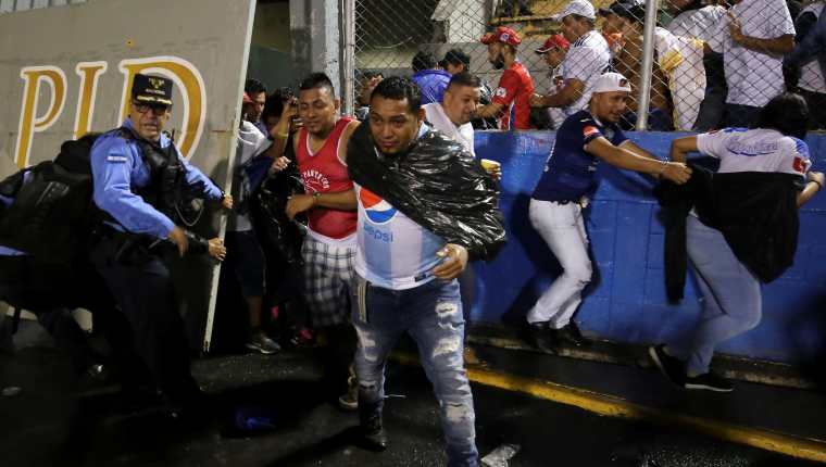 Aficionados ingresan al campo y se protegen de los gases lacrimógenos lanzados por las autoridades, debido a los disturbios a las afueras del Estadio Nacional por la cancelación del clásico entre Olimpia y Motagua. (Foto Prensa Libre: EFE)