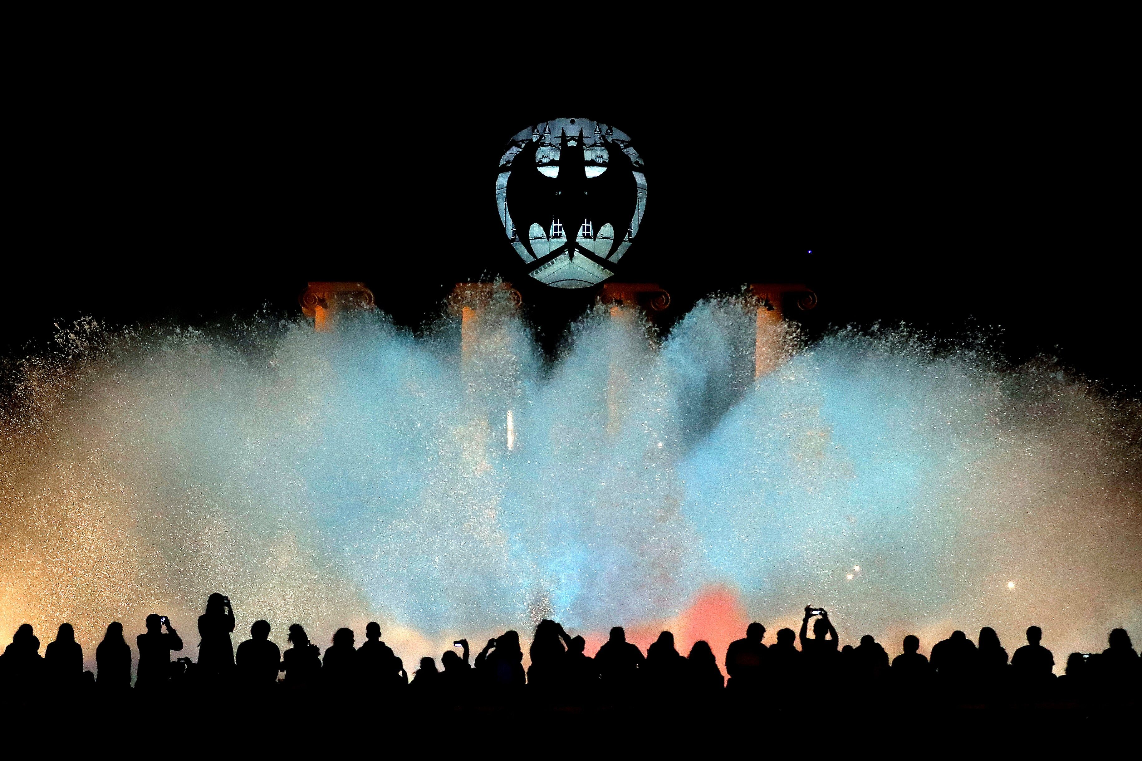 Centenares de personas observan el espectáculo de la Fuente Mágica de Montjuic mientras en la cúpula del Museu Nacional d'Art de Catalunya (MNAC), en Barcelona, se observa la "Batiseñal", el símbolo de Batman, que se proyectará en una catorcena de ciudades de todo el mundo por el 80 aniversario del Caballero Oscuro. (Foto Prensa Libre: EFE) 