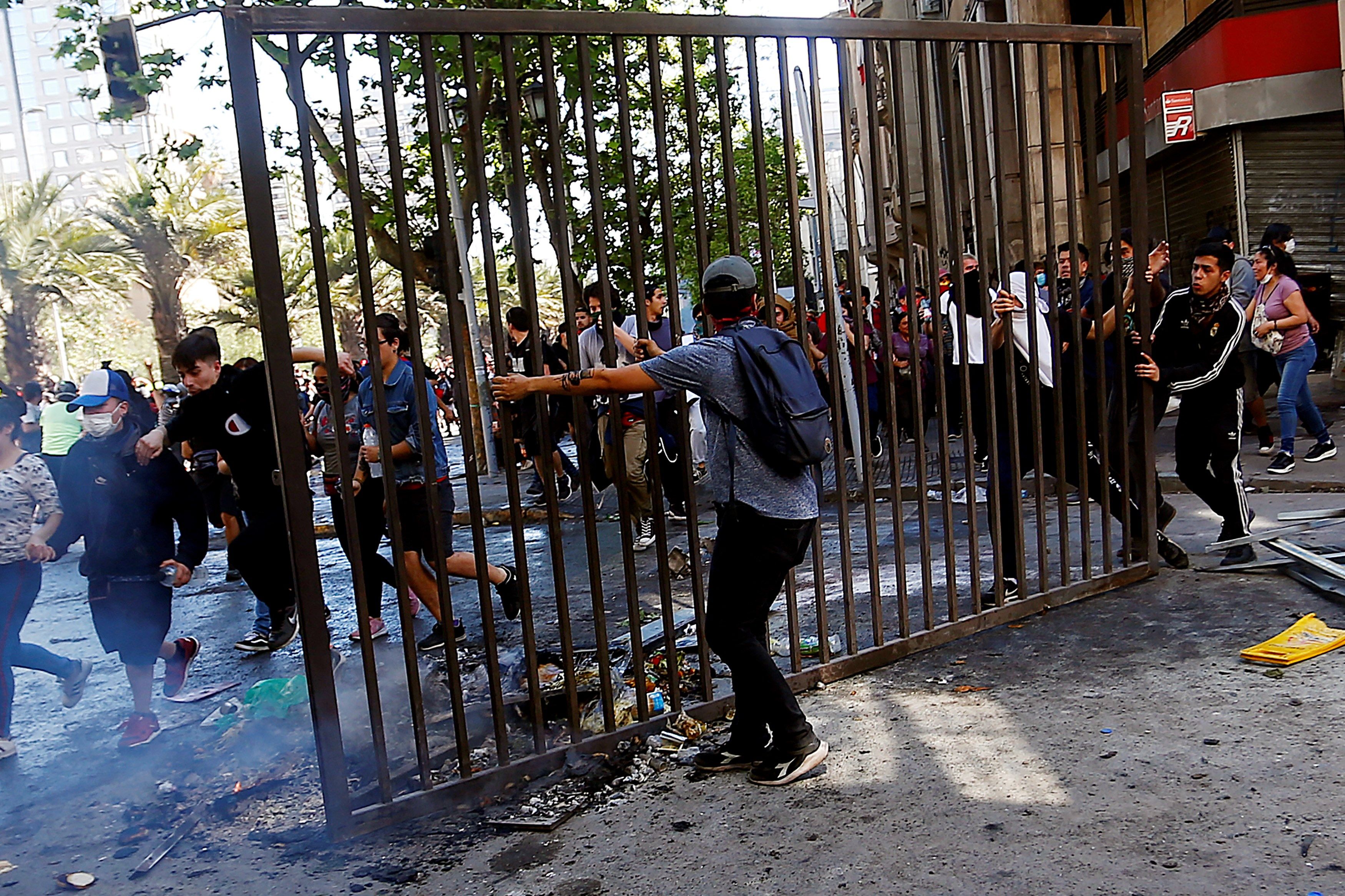 Manifestantes sacan una reja para ser lanzada a una barricada en el centro de la capital, sector Plaza Italia, durante una nueva jornada de masivas protestas en Santiago. (Foto Prensa Libre: EFE)