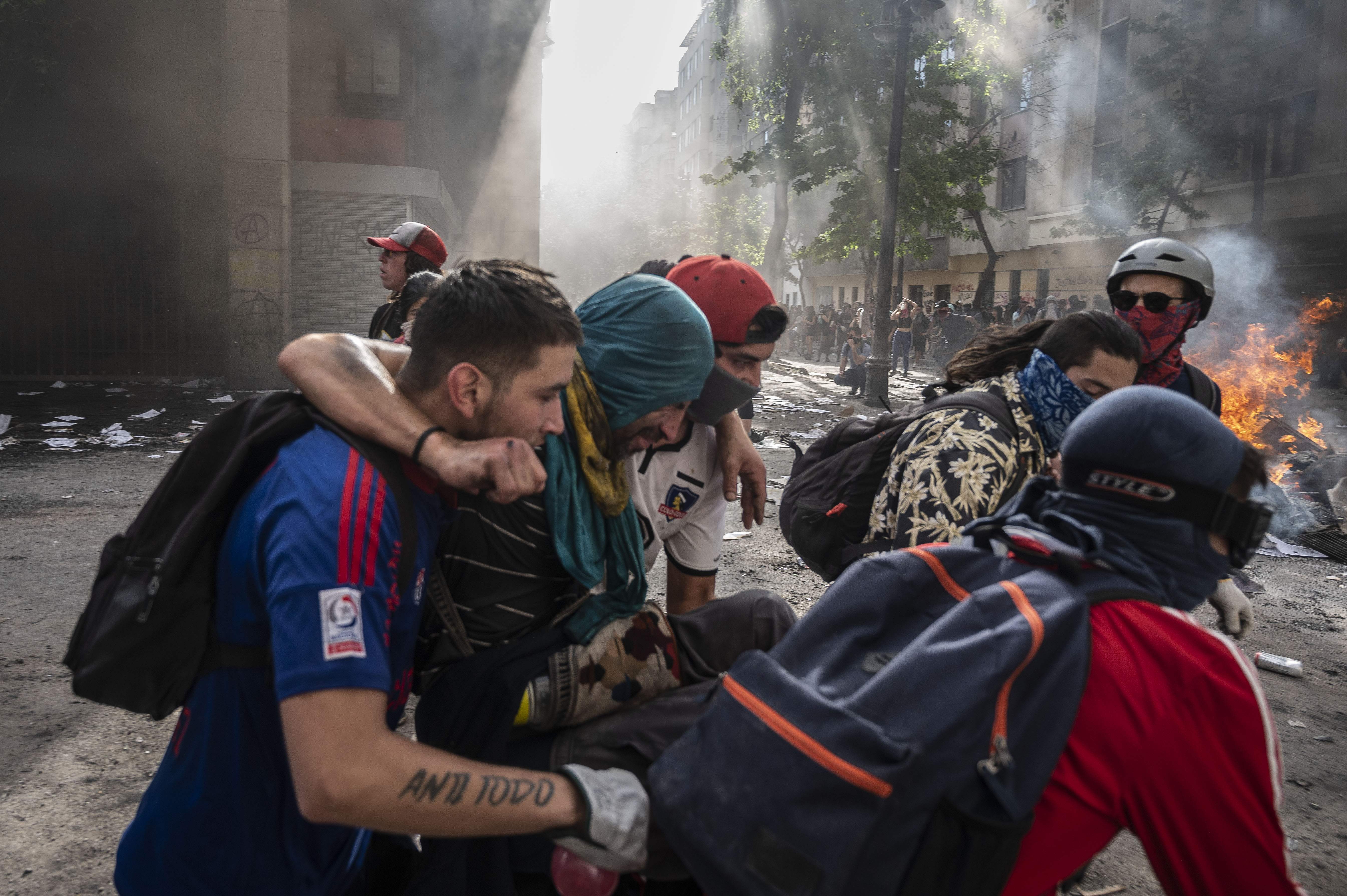 En la Plaza Italia, manifestantes ayudan a otro manifestante en apuros durante el quinto día consecutivo de protestas que estalló por un alza ahora suspendida en los precios de los boletos del metro. (Foto Prensa Libre: AFP)