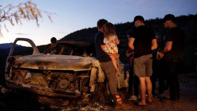 Los familiares de las víctimas frente a uno de los vehículos que resultó incendiado en la emboscada.