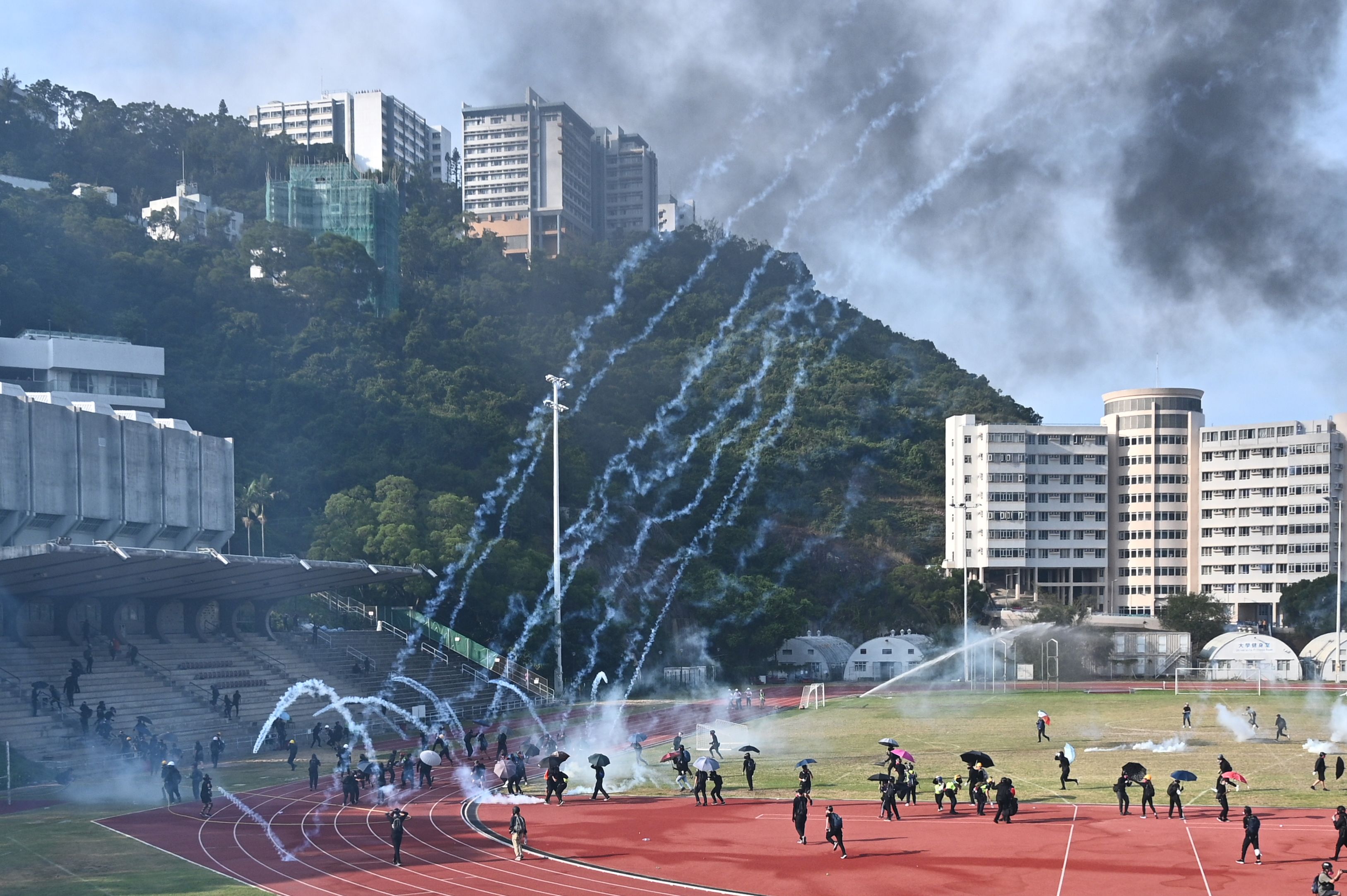 Protestantes corren mientras las bombas de gas caen en la Universidad  de Hong Kong (CUHK). (Foto Prensa Libre: AFP)
