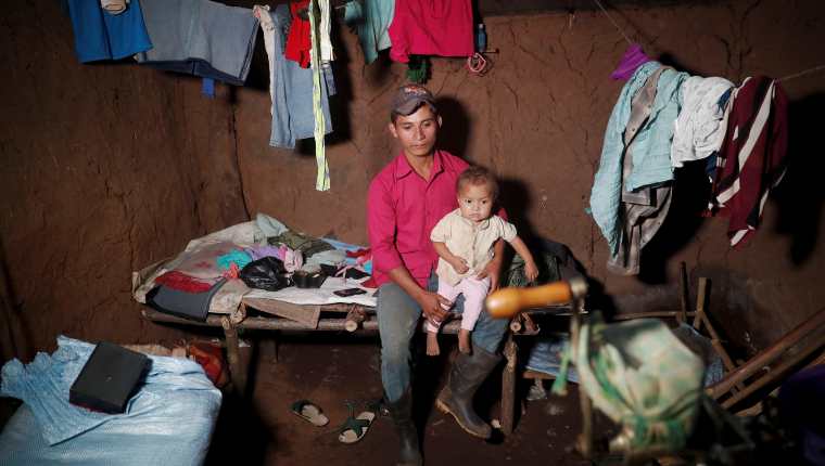 La niña Carla, de 4 años, es cargada por su padre adoptivo, Roque, en la única habitación de su casa de adobe y tierra, en el caserío El Ceibal, Jocotán, Chiquimula. (Foto Prensa Libre: EFE)
