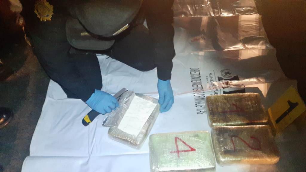 Un agente de la Policía inspecciona uno de los cuatro paquetes con cocaína. (Foto Prensa Libre: PNC) 
