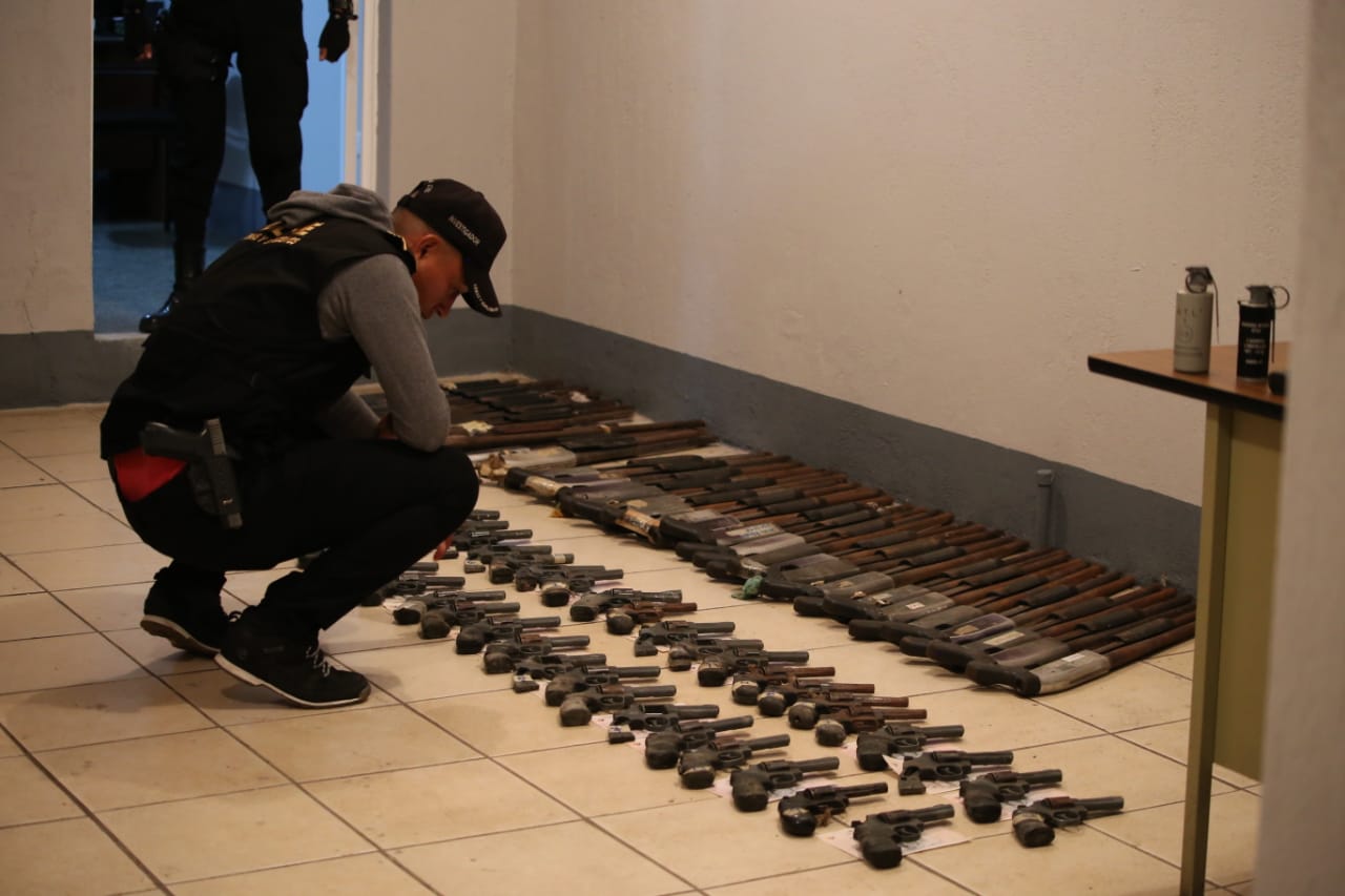 Un agente de la PNC revisa parte de las armas incautadas. (Foto Prensa Libre: PNC)