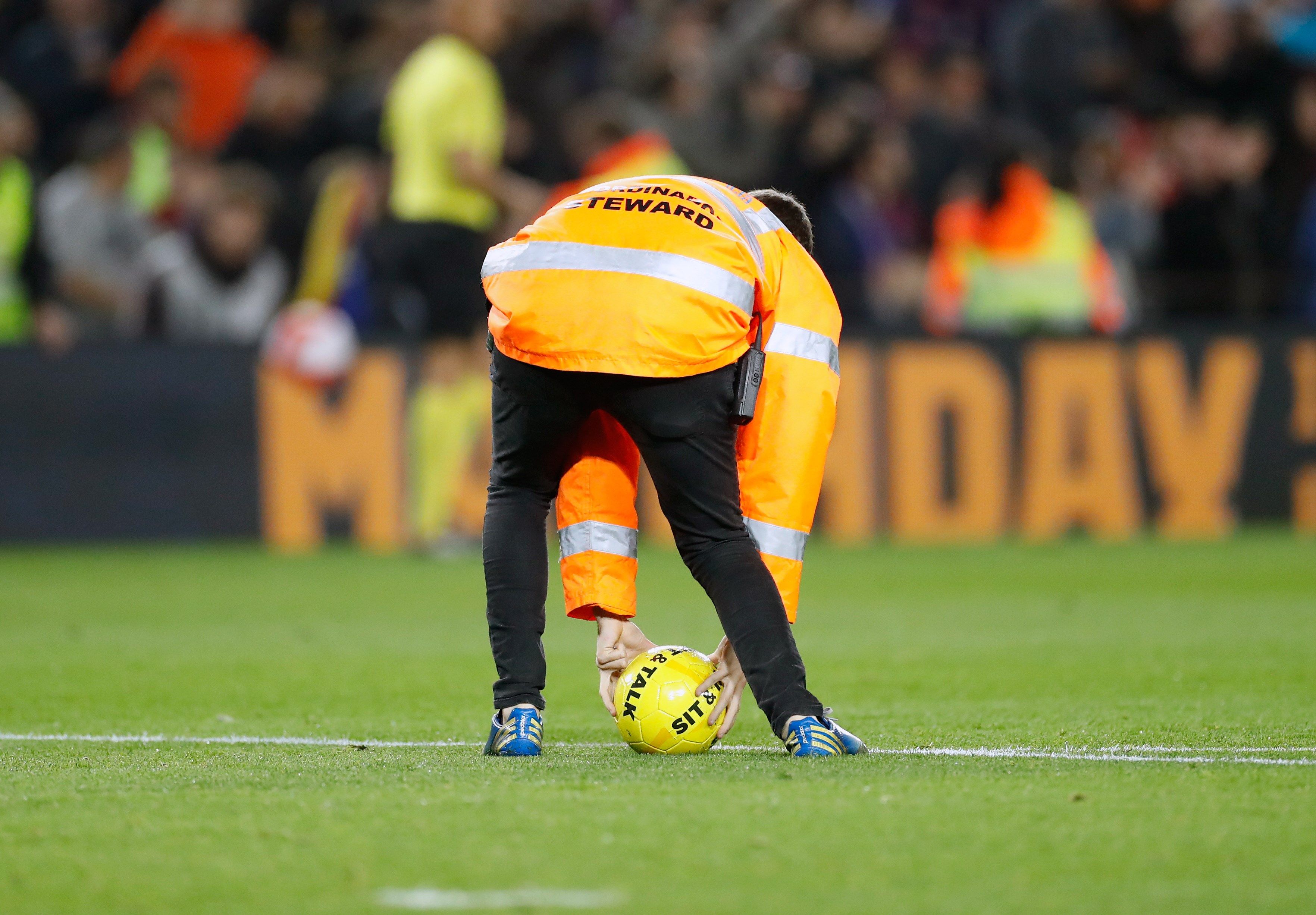 Un miembro de seguridad recoge una de las pelotas con el lema "Sit And Talk" lanzadas al cesped del Camp Nou. (Foto Prensa Libre: EFE)