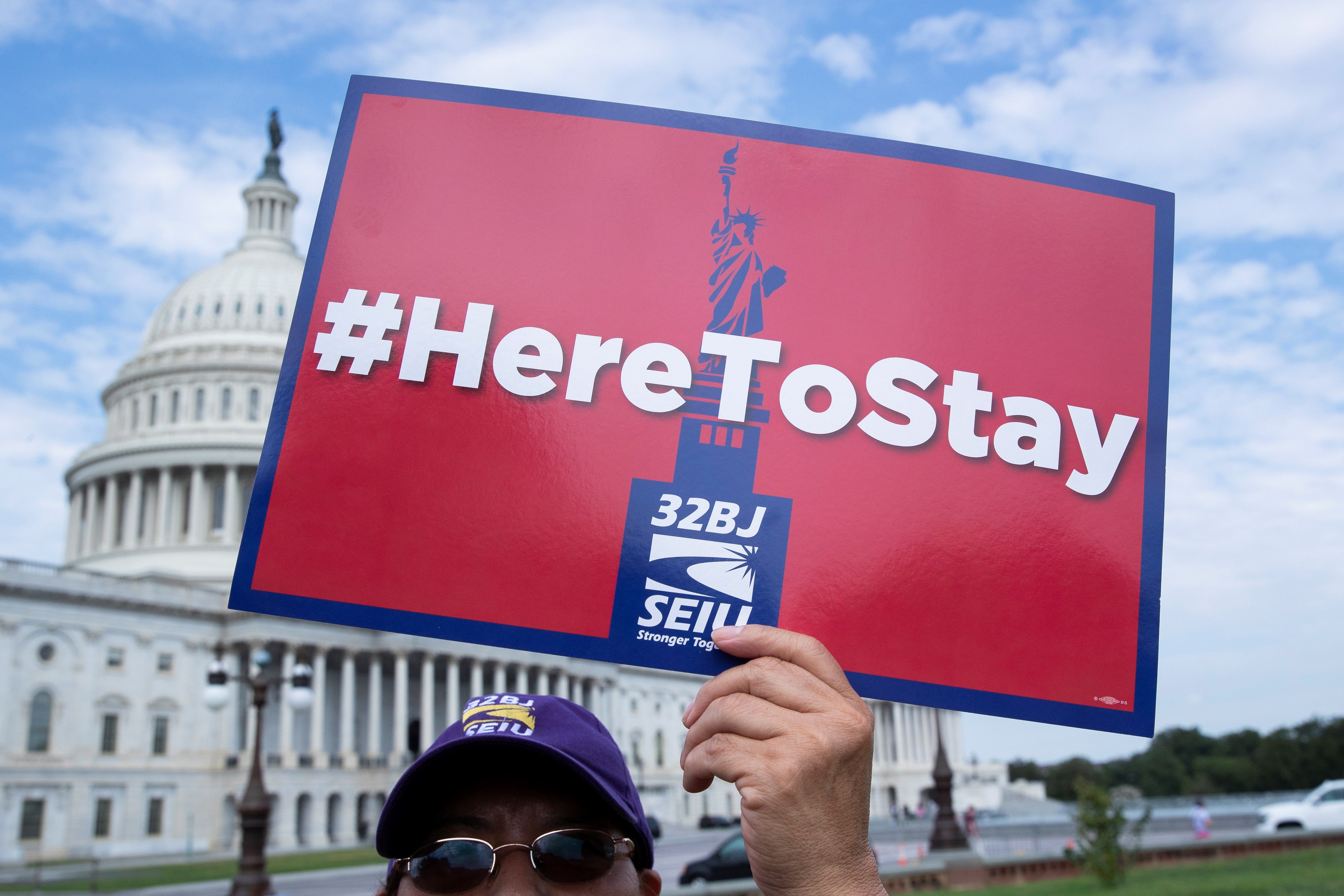 Fotografía de archivo del 9 de septiembre de 2019 donde aparece una persona mientras sostiene un cartel que dice "Aquí para quedarnos", durante una manifestación de inmigrantes enfrente del Capitolio en Washington. (Foto Prensa Libre: EFE)