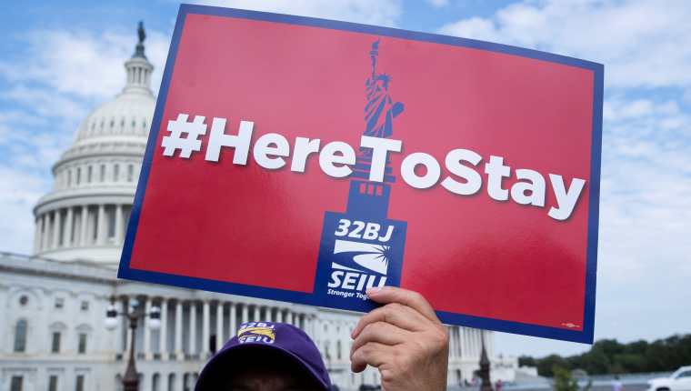 Fotografía de archivo del 9 de septiembre de 2019 donde aparece una persona mientras sostiene un cartel que dice "Aquí para quedarnos", durante una manifestación de inmigrantes enfrente del Capitolio en Washington. (Foto Prensa Libre: EFE)