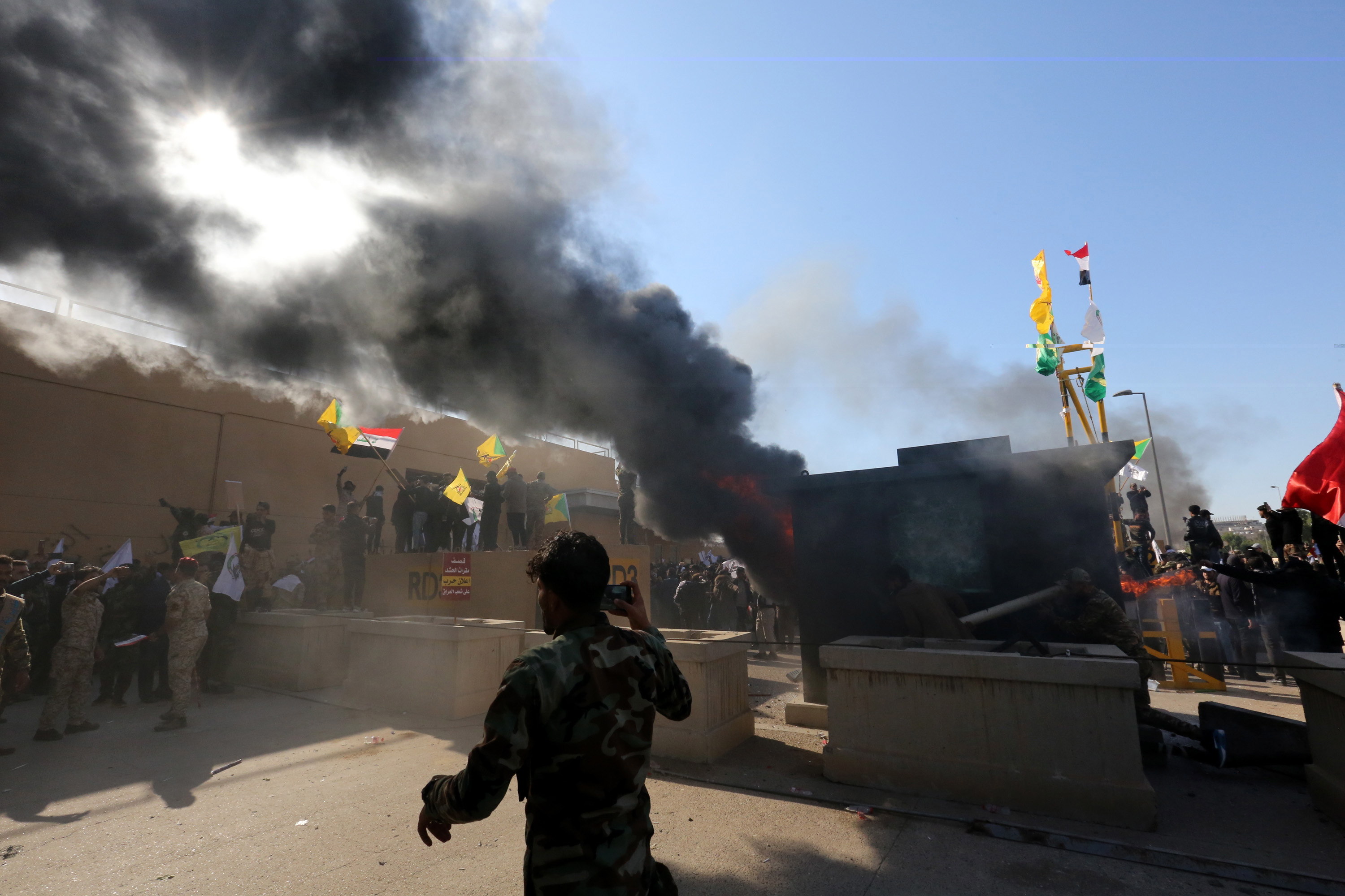 Miembros del grupo armado chiíta iraquí 'Fuerzas de movilización popular' y sus partidarios atacan a la embajada de EE. UU. Cuando el humo sale de su entrada en Bagdad, Iraq. (Foto Prensa Libre: EFE)