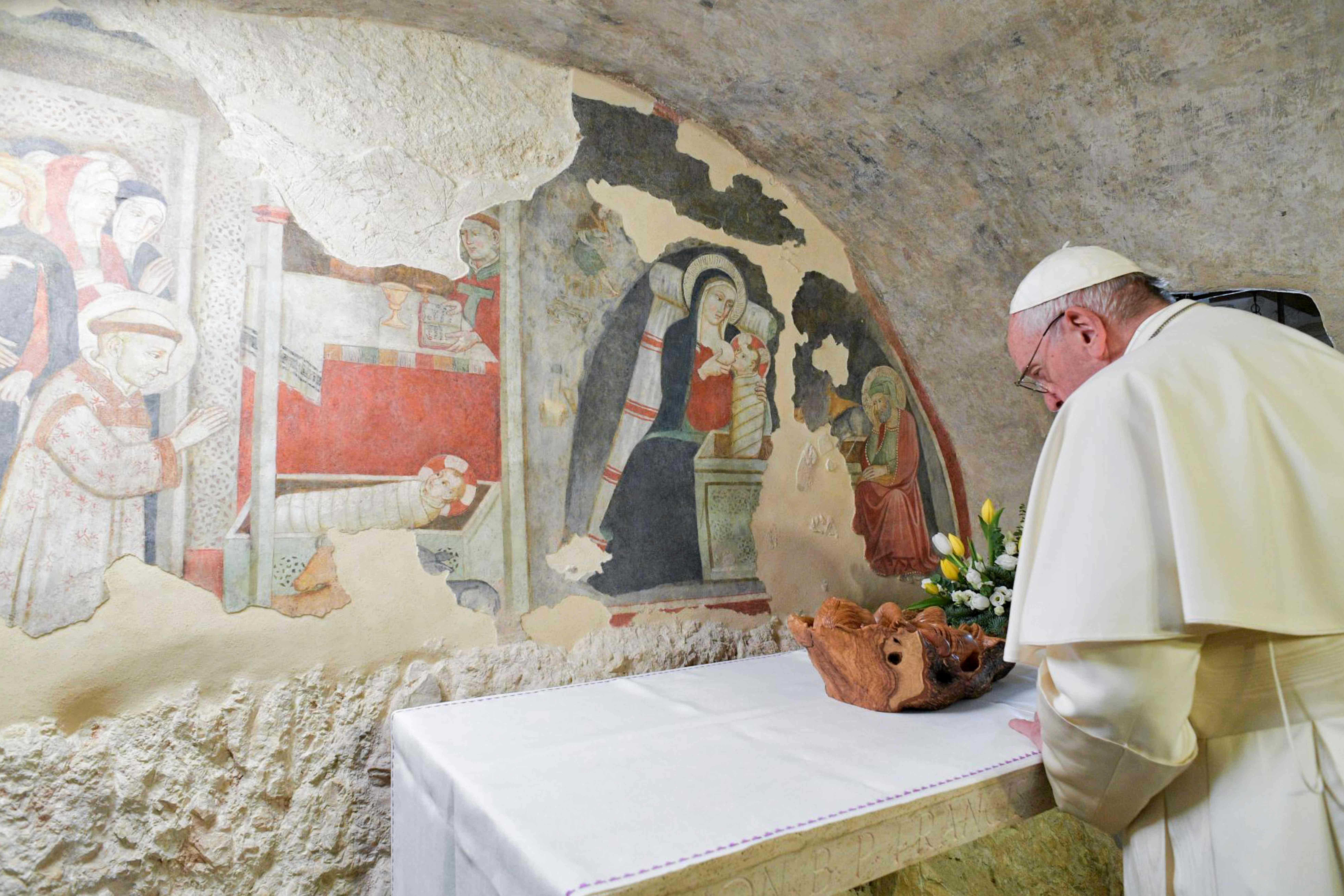 El papa Francisco ora frente a los frescos de la Natividad en la ciudad de el Greccio. (Foto Prensa Libre: AFP)